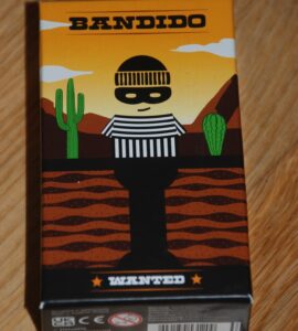 Colorful packaging of the board game "Bandido," featuring a cartoonish bandit character in a striped outfit against a desert backdrop with cacti and mountains. The box is labeled "WANTED" and showcases a playful art style.