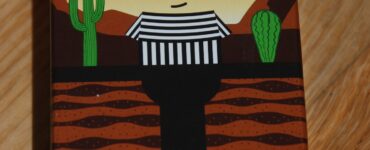 Colorful packaging of the board game "Bandido," featuring a cartoonish bandit character in a striped outfit against a desert backdrop with cacti and mountains. The box is labeled "WANTED" and showcases a playful art style.