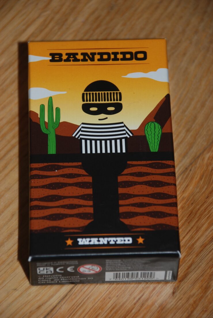 Colorful packaging of the board game "Bandido," featuring a cartoonish bandit character in a striped outfit against a desert backdrop with cacti and mountains. The box is labeled "WANTED" and showcases a playful art style.