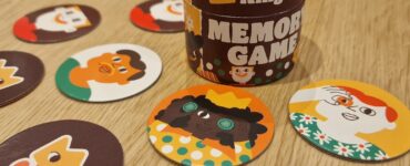 Colorful King Jr. memory game featuring a cylindrical container and various character-themed cards laid out on a wooden table, designed to enhance memory skills and provide family-friendly entertainment.