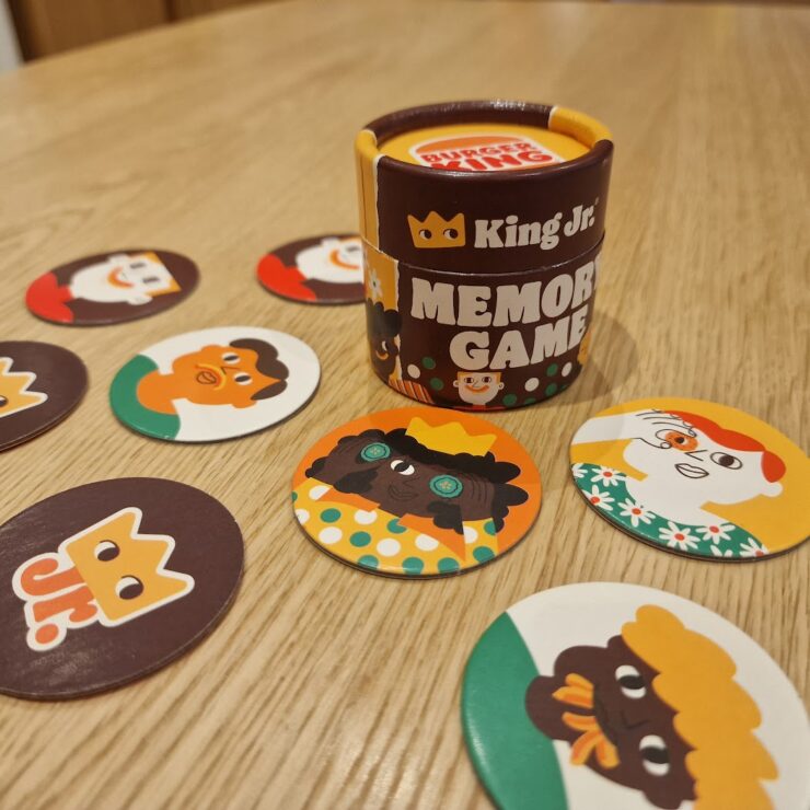 Colorful King Jr. memory game featuring a cylindrical container and various character-themed cards laid out on a wooden table, designed to enhance memory skills and provide family-friendly entertainment.