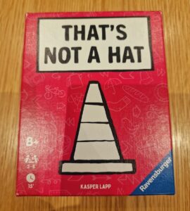 Box of the game "That's Not a Hat" by Kasper Lapp, featuring a playful design with a traffic cone illustration on a bright red background. Suitable for ages 8 and up, designed for 3 to 8 players with an estimated playtime of 15 minutes.