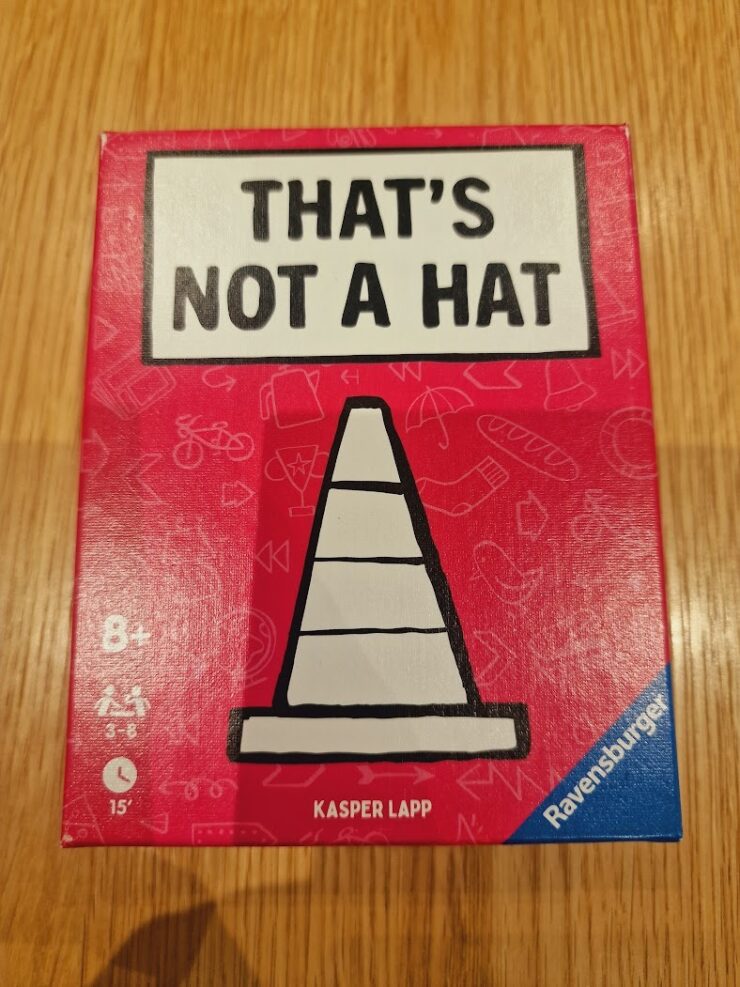 Box of the game "That's Not a Hat" by Kasper Lapp, featuring a playful design with a traffic cone illustration on a bright red background. Suitable for ages 8 and up, designed for 3 to 8 players with an estimated playtime of 15 minutes.