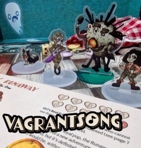 Vagrantsong tabletop game components featuring colorful acrylic character standees, including a dog, a female character with a weapon, and a quirky monster, set against a game board with dice and a character sheet.