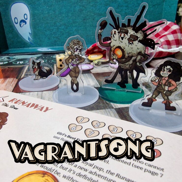 Vagrantsong tabletop game components featuring colorful acrylic character standees, including a dog, a female character with a weapon, and a quirky monster, set against a game board with dice and a character sheet.