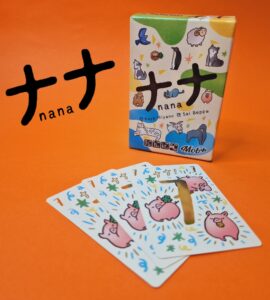 Colorful card game "Nana" by Kaya Miyano and Sai Beppu displayed with its box and several illustrated cards featuring cute animal designs on an orange background.