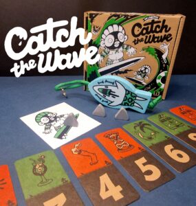 Colorful board game "Catch the Wave" featuring game components including cards, a character illustration, and game pieces, displayed with a playful design on a blue background.