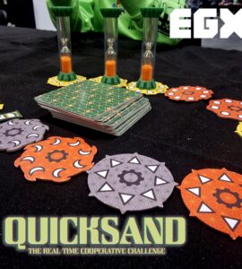 Image of the board game "Quicksand" displayed at EGX, featuring colorful game pieces including hexagonal tokens and hourglasses, highlighting the cooperative gameplay and real-time challenge elements.