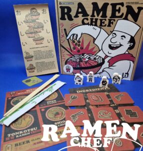 Ramen Chef board game components displayed, including the game box, instruction booklet, ingredient cards, character tokens, and chopsticks on a blue background. The design features vibrant illustrations related to ramen cooking, enhancing the game's culinary theme.