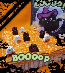 Colorful Halloween-themed board game setup featuring cute cat game pieces, including black and white cats in costumes, on an orange quilted board. The game, titled "Boooop," is designed by Scott Brady, with a festive background of bats and pumpkins. Perfect for family fun during the Halloween season.