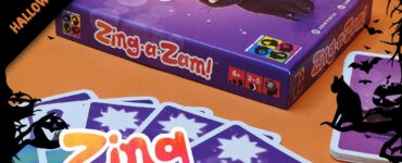 Halloween-themed game "Zing-a-Zam!" displayed with colorful cards and a purple box featuring a playful black cat, suitable for 2-5 players aged 6 and up. Perfect for festive gatherings and family game nights.