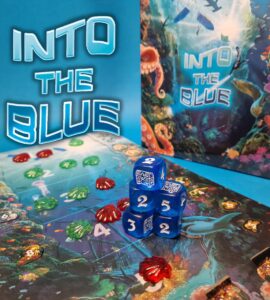 Colorful game setup for "Into the Blue," featuring a vibrant underwater-themed game board, decorative tokens in red and green, and blue dice displaying various numbers. The background highlights the game's title, surrounded by marine life illustrations.