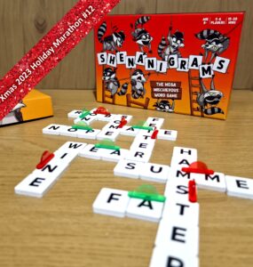 Colorful board game "Shenanigrams" displayed with letter tiles forming words on a wooden table, featuring a playful raccoon theme. Ideal for 2-6 players, ages 8 and up, with a gameplay time of 15-30 minutes. Part of the Xmas 2023 Holiday Marathon.
