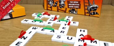 Colorful board game "Shenanigrams" displayed with letter tiles forming words on a wooden table, featuring a playful raccoon theme. Ideal for 2-6 players, ages 8 and up, with a gameplay time of 15-30 minutes. Part of the Xmas 2023 Holiday Marathon.