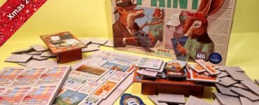 Board game "Fit to Print" by Peter McPherson displayed on a yellow background, featuring game components like cards, a score sheet, and numerous paper tiles. The game cover showcases illustrated animal characters, highlighting its theme and design.