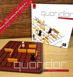 Mini Quoridor board game by Mirko Marchesi displayed on a wooden surface, featuring a brown game board with wooden barriers and player pieces. The game box is in the background, highlighting its design. Text overlay indicates "Xmas 2023 Holiday Marathon #11."