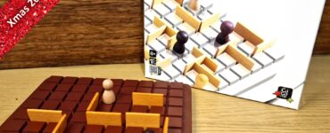 Mini Quoridor board game by Mirko Marchesi displayed on a wooden surface, featuring a brown game board with wooden barriers and player pieces. The game box is in the background, highlighting its design. Text overlay indicates "Xmas 2023 Holiday Marathon #11."