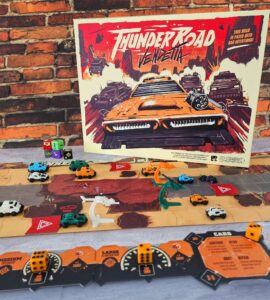 Thunder Road Vendetta board game setup featuring colorful miniature vehicles on a dynamic game board, with the game's vibrant cover art displayed prominently in the background against a brick wall. The scene showcases gameplay elements like dice and player cards, emphasizing the strategic and competitive nature of the game.