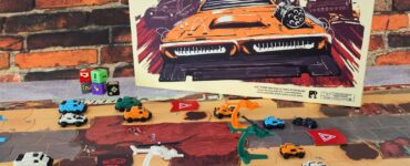Thunder Road Vendetta board game setup featuring colorful miniature vehicles on a dynamic game board, with the game's vibrant cover art displayed prominently in the background against a brick wall. The scene showcases gameplay elements like dice and player cards, emphasizing the strategic and competitive nature of the game.