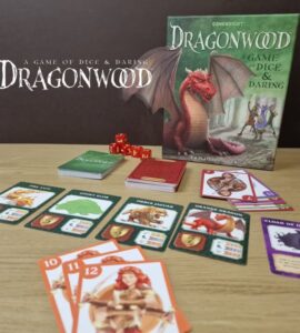 Game board of Dragonwood, a tabletop game featuring colorful cards and dice. The image shows the game box, various character and creature cards, and red dice on a wooden table. Ideal for 2-4 players aged 8 and up, Dragonwood combines strategy and luck in a fantasy setting.