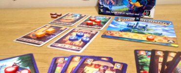 Board game "Once Upon a Plunder" displayed on a wooden table, featuring the game box, character cards, and colorful game tokens. The image showcases gameplay elements, including cards with various illustrations and point values, emphasizing the cooperative and competitive nature of the game.