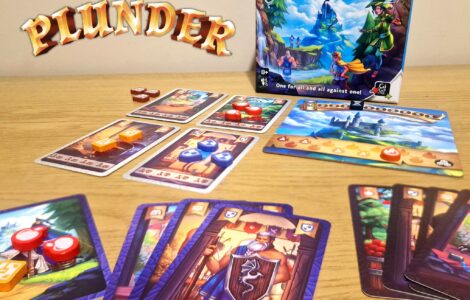 Board game "Once Upon a Plunder" displayed on a wooden table, featuring the game box, character cards, and colorful game tokens. The image showcases gameplay elements, including cards with various illustrations and point values, emphasizing the cooperative and competitive nature of the game.