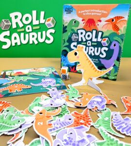 Colorful game components of "Roll-a-Saurus," a fun introductory dice game featuring dinosaur-themed cards and figures, with a vibrant game box in the background.