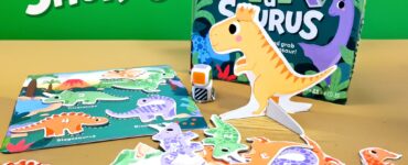Colorful game components of "Roll-a-Saurus," a fun introductory dice game featuring dinosaur-themed cards and figures, with a vibrant game box in the background.