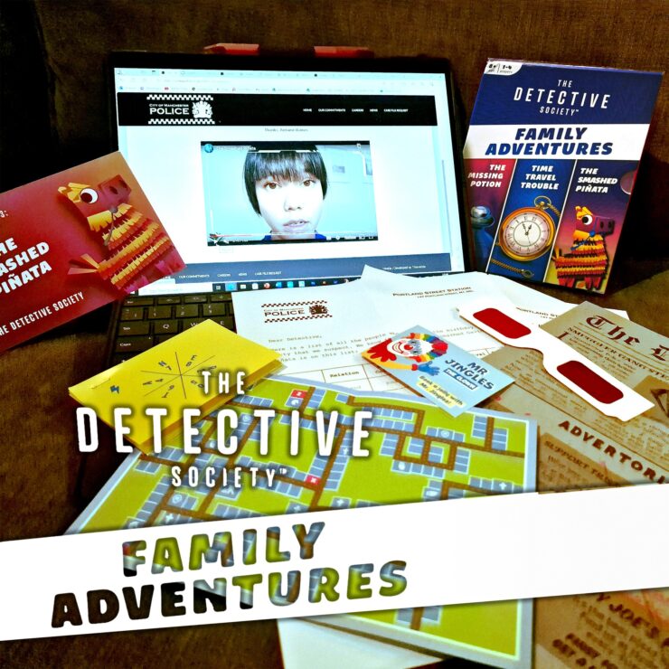 An interactive setup for "The Detective Society: Family Adventures," featuring a laptop displaying a video, game cards, a colorful map, and various clues, all designed for family-friendly mystery-solving activities.