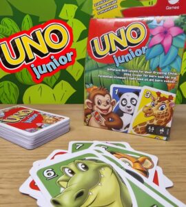 UNO Junior card game packaging displayed with colorful animal-themed cards. The box features characters like a monkey, panda, and giraffe, emphasizing different skill levels for children. The game encourages fun and learning for young players, with a vibrant background of green leaves.