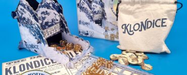 Klondice board game setup featuring the game box, dice, scoring sheet, and a drawstring bag. The game includes a unique mountain-themed design and components for players to stake their claim and earn credits. Ideal for family game nights and strategy enthusiasts.