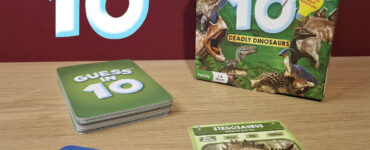 Colorful image of the "Guess in 10: Deadly Dinosaurs" game by Skillmatics, featuring the game box, clue cards, and a Stegosaurus information card. Ideal for family game nights, suitable for 2-6 players aged 8 to 99.