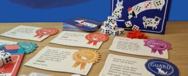 Colorful board game "Spots" featuring dice, action cards, and playful dog illustrations. The image showcases the game components laid out on a wooden surface with a vibrant blue background, highlighting the game's engaging design and mechanics. Perfect for family game night or gatherings.