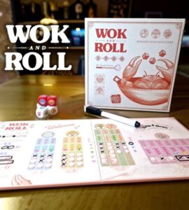 Wok and Roll board game displayed on a wooden table, featuring the game box, colorful dice, and player score sheets. The design highlights modern Asian themes and gameplay elements, suitable for family and friends.