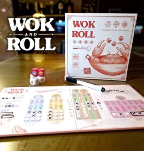 Wok and Roll board game displayed on a wooden table, featuring the game box, colorful dice, and player score sheets. The design highlights modern Asian themes and gameplay elements, suitable for family and friends.