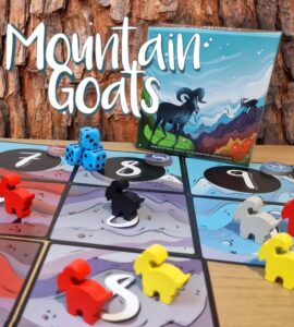 Colorful game pieces and dice are displayed on a board for the game "Mountain Goats," featuring a vibrant cover illustration of a goat on a mountain landscape.