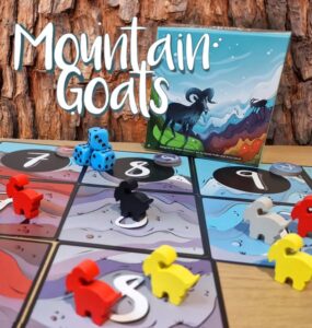 Colorful game pieces and dice are displayed on a board for the game "Mountain Goats," featuring a vibrant cover illustration of a goat on a mountain landscape.