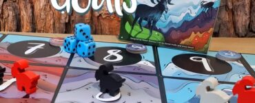 Colorful game pieces and dice are displayed on a board for the game "Mountain Goats," featuring a vibrant cover illustration of a goat on a mountain landscape.