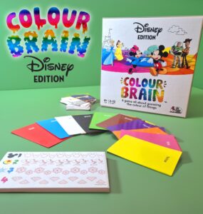 Colour Brain Disney Edition board game displayed on a green background, featuring colorful question cards, answer cards, and a game box with iconic Disney characters. Suitable for 2 to 12 players aged 8 and up, this game challenges players to guess the colors of various Disney-themed items.
