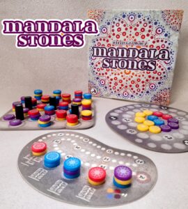 Colorful game components of "Mandala Stones," including various tokens and scoring boards, displayed alongside the game box featuring intricate designs. Ideal for family game nights and strategy lovers.