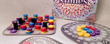 Colorful game components of "Mandala Stones," including various tokens and scoring boards, displayed alongside the game box featuring intricate designs. Ideal for family game nights and strategy lovers.