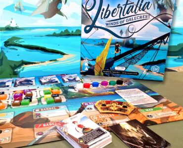 Image of the board game "Libertalia: Winds of Galecrest," featuring the game box, game cards, and various player tokens on a colorful game board. The background showcases a vibrant seascape with ships and islands, emphasizing the maritime theme of the game.