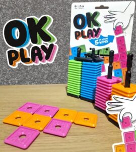 Colorful stacking game "OK Play" featuring vibrant blocks in pink, orange, green, and blue. The game encourages strategic thinking as players aim to connect five blocks in a row. Ideal for 2-4 players aged 6 and up, the packaging showcases the game design and instructions.