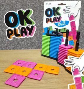 Colorful stacking game "OK Play" featuring vibrant blocks in pink, orange, green, and blue. The game encourages strategic thinking as players aim to connect five blocks in a row. Ideal for 2-4 players aged 6 and up, the packaging showcases the game design and instructions.