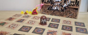 An image depicting the board game "Tokyo Poo Divers," featuring the game box, game pieces, and cards laid out on a wooden surface. The colorful design includes a cartoon diver, playful tokens, and various illustrated cards, showcasing the game's fun and quirky theme.