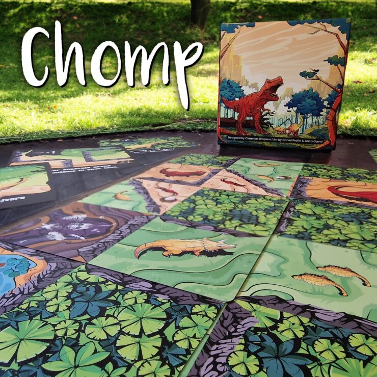 Colorful game board of "Chomp," featuring illustrated dinosaur-themed tiles laid out on a grassy surface, with the game's box displayed in the background.