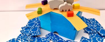 Colorful game setup for "Rafter Five," featuring a blue box with wooden animal figures and vibrant building pieces scattered around.