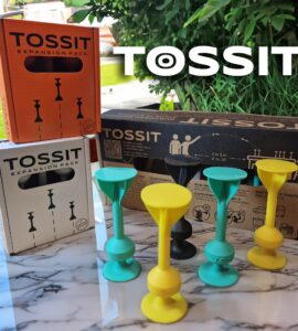 TOSSIT game expansion packs displayed on a marble surface, featuring colorful game pieces in yellow, green, and black, alongside packaging in orange and white, designed for interactive gameplay with options for 2 to 6 players.