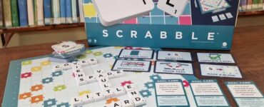 Scrabble Together game box displayed with game pieces and board, featuring colorful tiles, goal cards, and letters, set against a library background. Perfect for family game nights and word enthusiasts.
