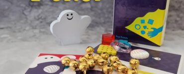 Image of the board game "Dro Polter," featuring a smiling ghost figure, colorful game cards with various designs, and game pieces including gold bells and a red block. The game box is visible, showcasing its vibrant artwork. Ideal for family game nights and fun gatherings.